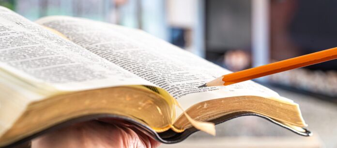 A man holds a Bible with a pencil, against the background of the living room. Reading a book in a cozy atmosphere.